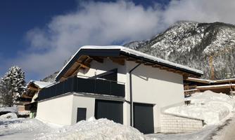 A modern house in a snowy landscape. In the background, mountains and a blue sky are visible.