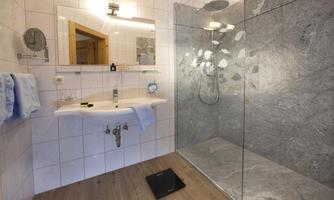 A modern bathroom with a glass shower and elegant stone tiles. White walls and a wooden floor create a bright, pleasant atmosphere.