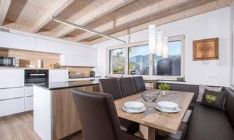 A modern kitchen with an edible table and elegant chairs. Large windows offer a view of the mountains.