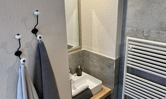 A modern bathroom with a sink and a large mirror. Towels are hanging on the wall and a towel warmer is visible.