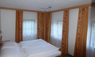 A cozy bedroom with a double bed and bright curtains. The walls are designed in warm colors, creating an inviting atmosphere.