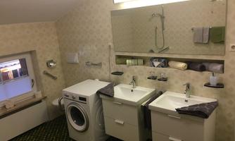 A modern bathroom with two sinks and a washing machine. There is a large mirror and decorative towels.
