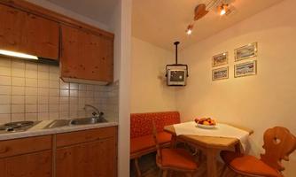 A cozy kitchen with wooden cabinets and a small dining area. The table is adorned with a fruit bowl and there is a bench and chairs.