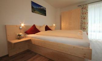 A cozy bedroom with a large bed and wood-paneled walls. The windows let in plenty of light, creating an inviting atmosphere.