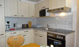 A modern kitchen with light wooden cabinets and a clear workspace. A bouquet of flowers and a placed tablecloth are on the table.