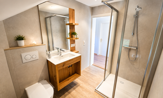 A modern bathroom with wood and stone accents. It features a sink, a shower, and a bright, friendly atmosphere.