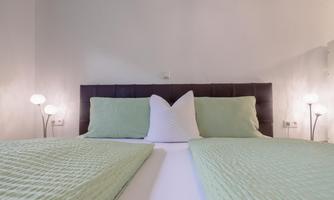 A cozy bedroom with a double bed and green bedspreads. Soft lamps create an inviting atmosphere.