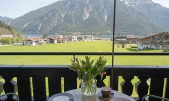 A picturesque view from a balcony of green meadows and mountains. On the table is a vase with tulips and dinnerware for two people.