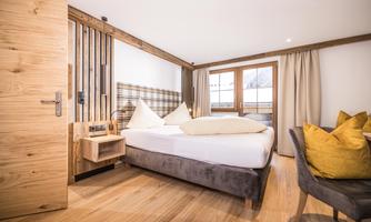 A modern hotel room with a large bed and a cozy wooden interior.  
Large windows provide plenty of daylight and a pleasant atmosphere.