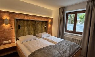 A modern bedroom with a double bed and stylish wooden details. Large windows provide plenty of daylight.