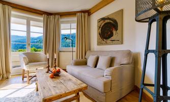 A cozy living room with a beige sofa, a wooden table, and a beautiful view of the landscape. Large windows with curtains and a modern design contribute to the stylish atmosphere.