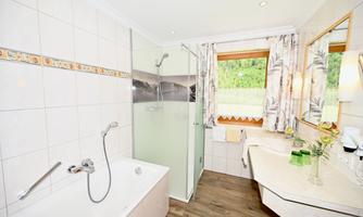 A modern bathroom with a bathtub and a separate shower. Large windows let in plenty of natural light and offer a view of the outdoor area.