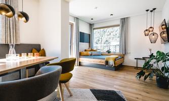 A modern living room with a dining area and a comfortable sofa bed. Large windows provide a view of nature and ensure plenty of light.