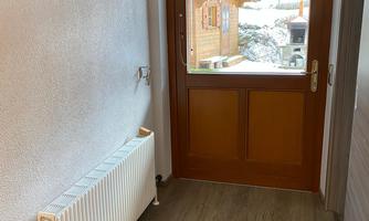 An inviting hallway with a wooden door and a radiator. The floor is decorated with a carpet in neutral colors.