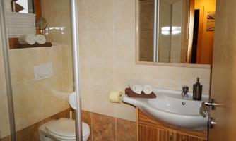 A modern bathroom with a shower, a sink, and a toilet. The walls are brightly tiled, and there are towels on a shelf.