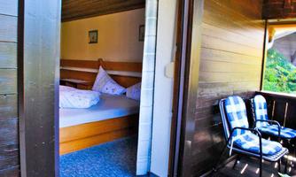 A cozy room with a bed and pillows. On the balcony are two chairs and the door is open for fresh air.