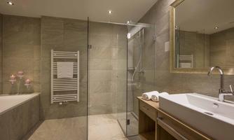 A modern bathroom with a glass shower and a bathtub. The walls are in neutral tones, and the sink has a wooden look.