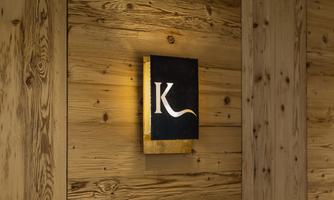 A modern sign with the letter "K" on a wooden panel. The sign is illuminated and creates a warm atmosphere.