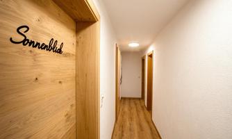 A bright hallway with wooden details and several doors. The door on the left side is labeled with the name "Sonnenblid."