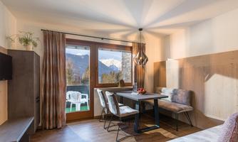 A modern living room with a dining table and comfortable chairs. Large windows offer a view of the mountains and provide plenty of daylight.
