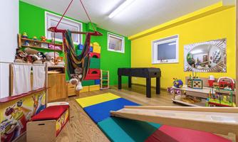 A child-friendly playroom with colorful walls in yellow and green. There are toys, a slide, and a hanging swing area.