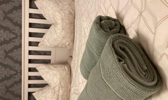 A cozy bed with striped pillows and discreet bedding. Two green towels are neatly placed on the bedspread.