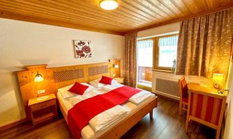 A cozy bedroom with a wooden ceiling and natural light. There is a large bed with red pillows and a desk next to a window.