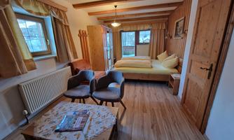 A cozy bedroom with two beds and rustic wood interiors. The room is bright and inviting, with a small table and chairs.