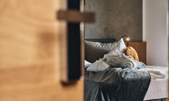 A cozy bedroom with a bed covered in blankets and pillows. Soft light creates an inviting atmosphere.