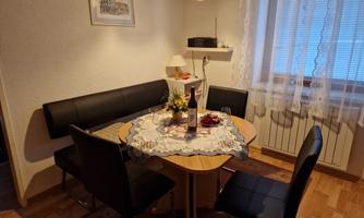 A cozy dining area with a round wooden table and black chairs. Flowers and a bottle of wine are arranged on the table.
