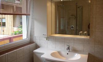 A modern bathroom with a white sink and a large mirror. The window lets in daylight and offers a view outside.