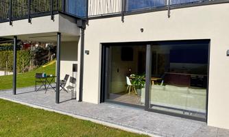A modern house with large windows and a porch. The garden is green and well-maintained, ideal for relaxed hours outdoors.