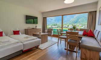A modern room with two beds and a dining area. The view of the mountains and nature is impressive.