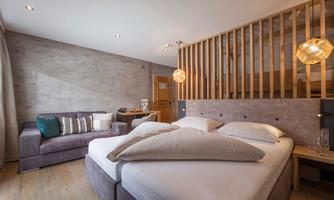 A modern bedroom with a comfortable bed and a seating area. The warm wood and gray tones create a cozy atmosphere.