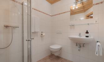 A modern bathroom with shower, sink, and toilet. Bright tiles and a wooden ceiling create a friendly atmosphere.