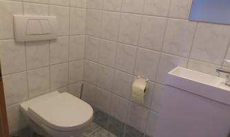A simple bathroom with white tiles. It includes a toilet and a sink with a mirror.