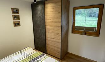 A cozy bedroom with a bed and a wooden wardrobe. The window offers a view of the green landscape.