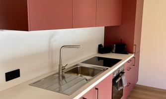 A modern kitchen with red cabinets and a light countertop. It includes a sink and a cooking surface.