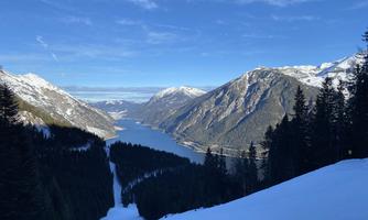 An impressive mountain landscape with snow-covered peaks and a sparkling lake. The sky is clear and blue, creating a tranquil atmosphere.