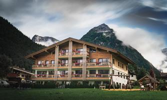 A modern hotel building in the Alps, surrounded by tall mountains. The sky is cloudy, and there is a playground in the foreground.