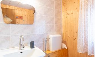 A bright bathroom with a sink, a toilet, and a small window. The walls are partially tiled and partially made of wood.