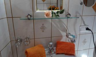 A modern bathroom with a handbasin and two orange towels. A glass shelf with a vase and flowers decorates the sink.