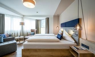 A modern bedroom with two beds and a cozy sitting area. Large windows provide plenty of daylight and a pleasant atmosphere.