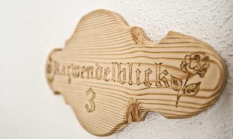 A wooden nameplate with the inscription "Kastanienblick 3". The sign has an elegant shape and a floral vine.
