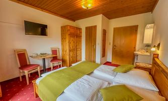 A cozy room with a double bed and two green cushions. There is a small table with chairs and a television on the wall.