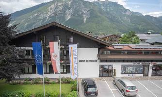 A charming house named "Haus Leithner," surrounded by beautiful countryside and mountains. The flags of the EU and Austria are flying in front of the building.