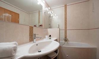 A modern bathroom with a sink, a shower, and a bathtub. The walls are brightly tiled and there are sanitary fixtures in neutral colors.