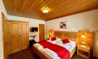 A cozy bedroom with a large double bed and wooden paneling. The room is bright and inviting, featuring a wardrobe and a dresser.