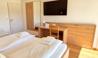 A modern bedroom with two beds and a desk. The room has a large mirror and a television on the wall.