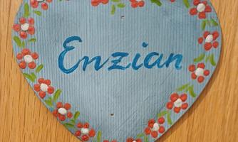 A heart-shaped sign in blue, adorned with red flowers. The word "Enzian" is written in blue text on it.